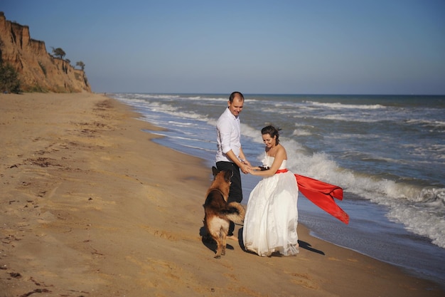 Casal de noivos caminha perto do mar com seu cão pastor alemão ao ar livre