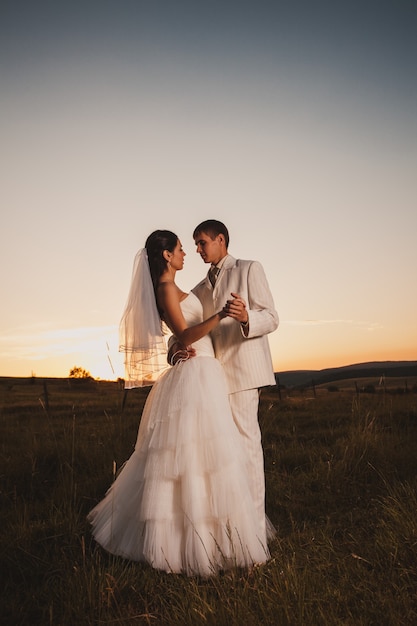 Casal de noivos dançando na colina ao pôr do sol