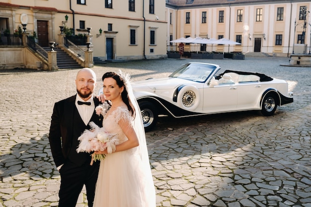 Casal de noivos elegantes no pátio do castelo perto de um carro retrô