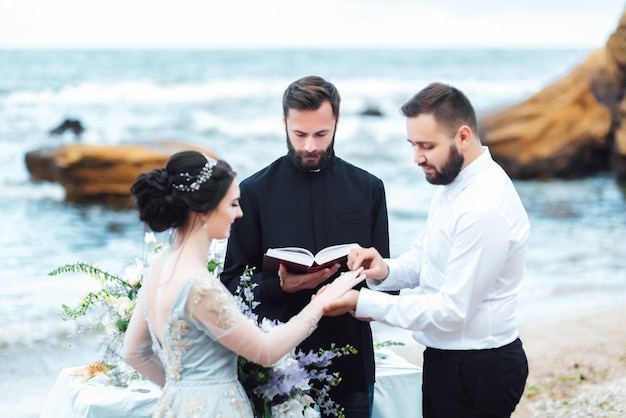 Casal de noivos perto do oceano com um padre