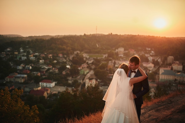Casal de noivos se abraçando ao pôr do sol