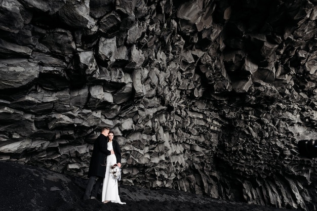 Casal de noivos sob uma rocha de pedras de basalto