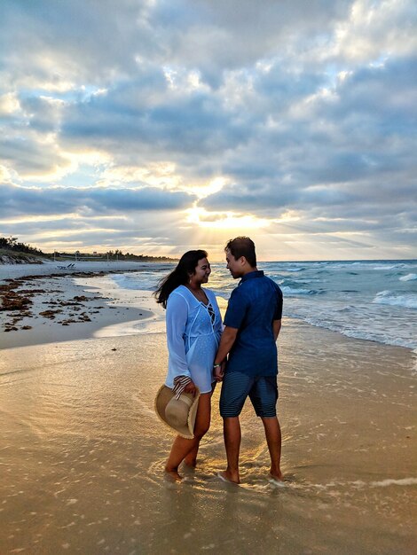 Casal de pé na praia contra o céu durante o pôr do sol