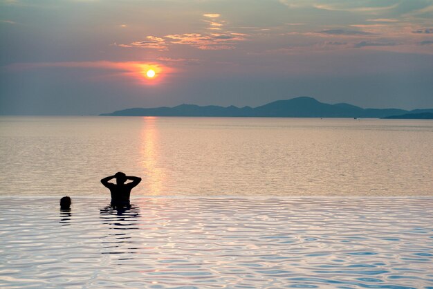 Casal de pessoas relaxando na piscina infinita e belo pôr do sol no mar em tempos de crepúsculo