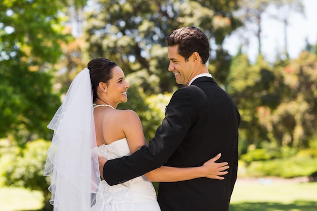 Casal de recém-casados ​​com braços ao redor no parque