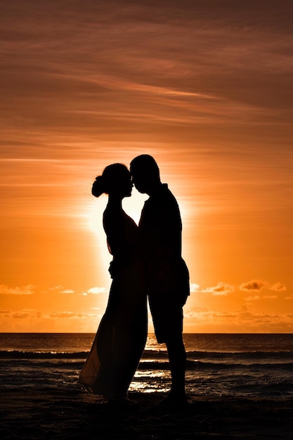 Casal de silhueta se abraçando na praia contra o céu laranja durante o pôr do sol