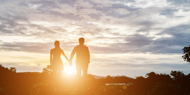 Foto casal de silhuetas de mãos dadas em terra contra o céu durante o pôr do sol