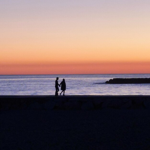 Casal de silhuetas na praia contra o céu durante o pôr do sol