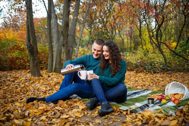 Foto casal de suéter bebe chá na floresta de outono