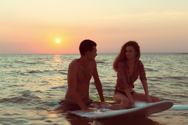 Casal de surf apoiando-se em pranchas de surf no mar