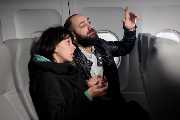 Casal de turistas esperando o voo para decolar no avião, sentados na classe econômica. Homem pedindo ajuda ao comissário de bordo, voando com avião das vias aéreas internacionais para viajar nas férias de férias.