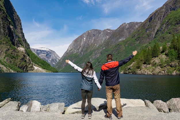 Casal de turistas no sopé do fiorde e rodeado por altas montanhas em Gudvangen Noruega