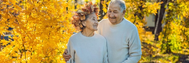 Casal de velhos feliz se divertindo no parque outono. Homem idoso vestindo uma coroa de folhas de outono para sua esposa idosa BANNER, FORMATO LONGO