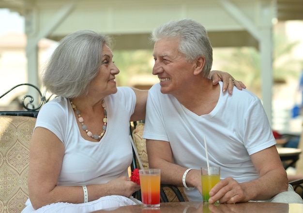 Casal de velhos sorridentes e divertidos bebendo suco em um café