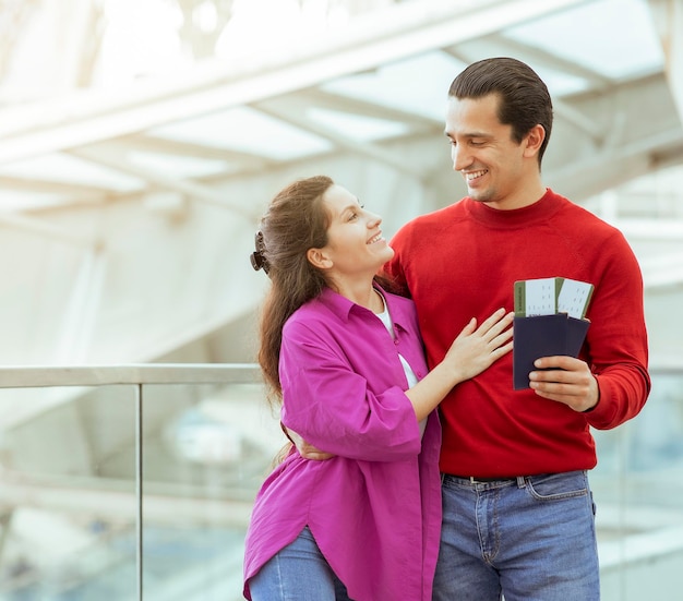 Casal de viajantes segurando passaporte e cartões de embarque se abraçando no aeroporto