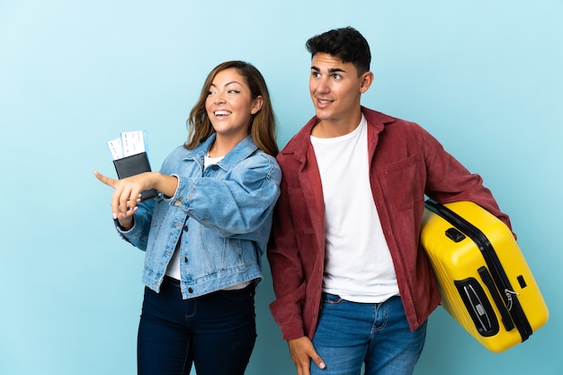 Casal de viajantes segurando uma mala em azul apontando para o lado para apresentar um produto