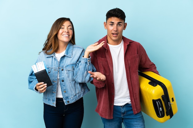 Casal de viajantes segurando uma mala em azul com expressão facial de surpresa e choque