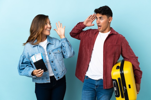 Casal de viajantes segurando uma mala em azul com expressão facial de surpresa e choque