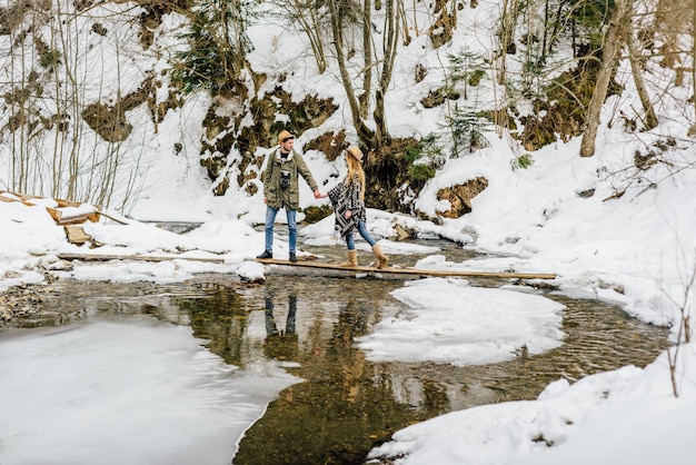 Casal de viajantes supera obstáculos, rio de montanha no inverno.