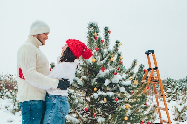 Casal decorando árvore de natal ao ar livre neve inverno ao ar livre