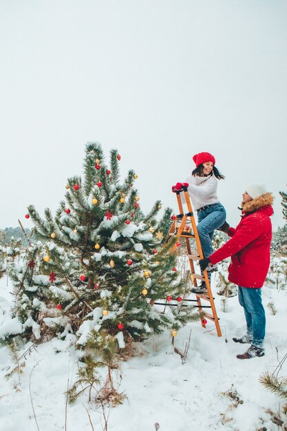 Casal decorando árvore de natal ao ar livre neve inverno ao ar livre