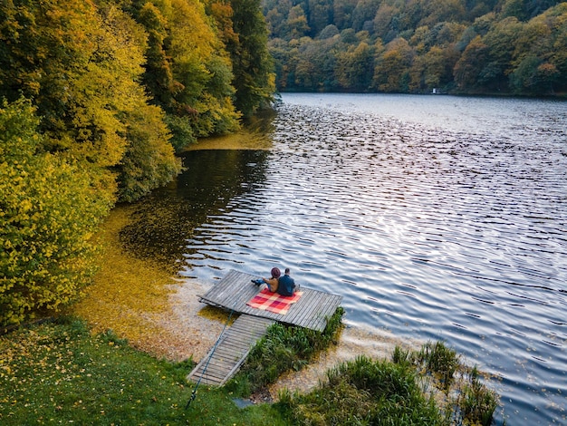 Casal deitado no cais no lago coberto com folhas de outono