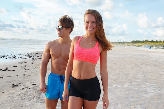 Casal desportivo de homem sem camisa e mulher posando na praia.