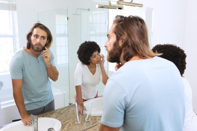 Casal diversificado em pé no banheiro aplicando creme facial