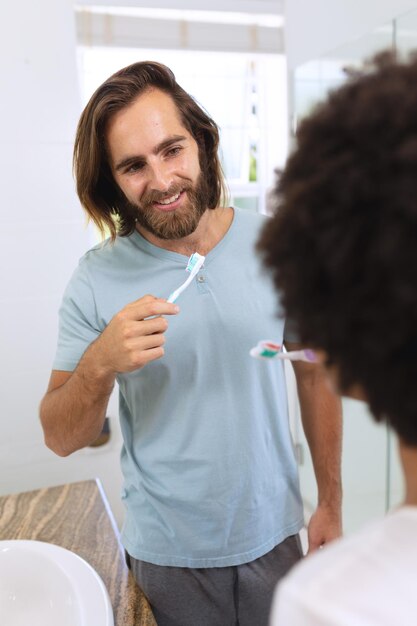 Foto casal diversificado em pé no banheiro escovando os dentes