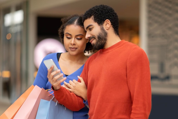 Casal diversificado fazendo compras on-line usando smartphone juntos no shopping ao ar livre