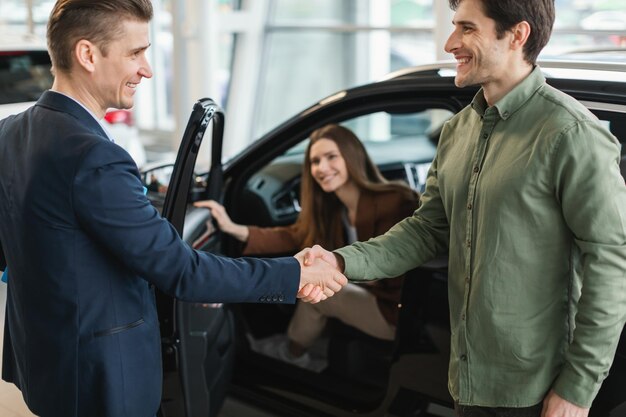 Casal do milênio apertando as mãos com vendedor de carros comprando novo veículo na concessionária