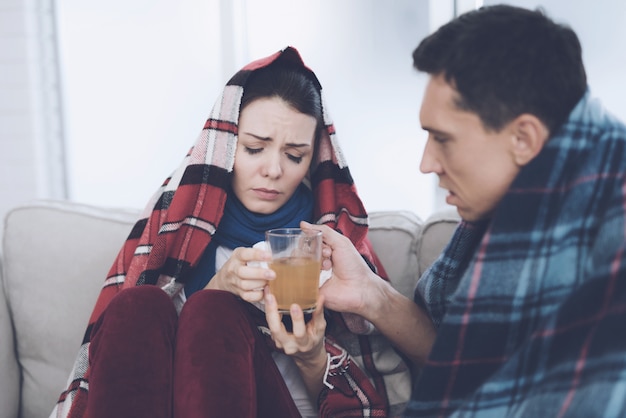 Casal doente está bebendo chá no sofá em casa.