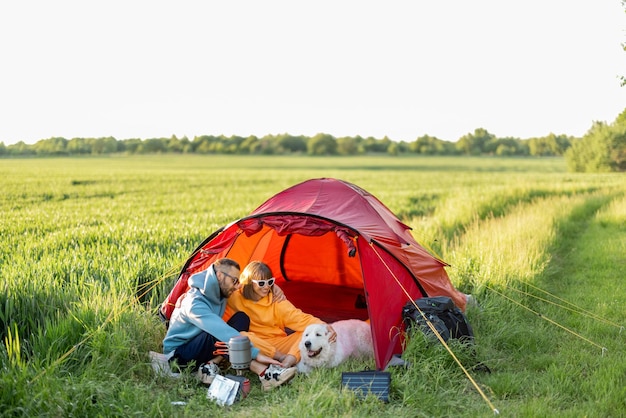 Casal e animal de estimação no acampamento com barraca em um campo verde