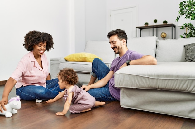 Casal e filha sorrindo confiante brincando com brinquedos sentados no chão em casa