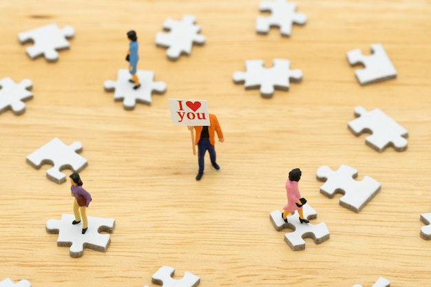 Casal em miniatura pessoas em pé com coração vermelho é a promessa de amor.