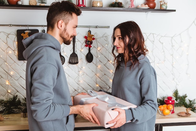 Casal em pé cozinha aberta presentes apresenta guirlandas em casa aconchegante atmosfera interior Ano Novo