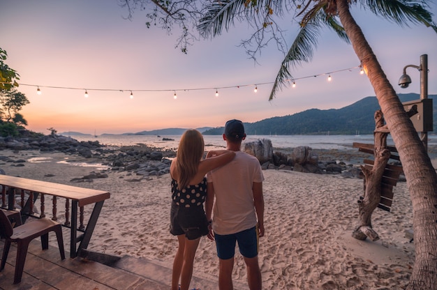 Casal em pé de turismo com pôr do sol na praia