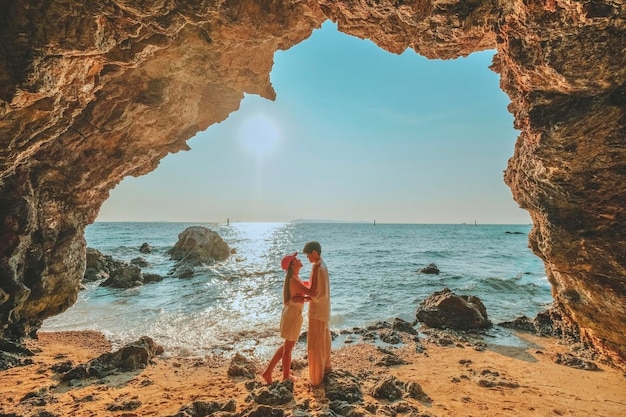 Casal em pé sobre uma rocha na entrada da caverna olhe para o mar e belas vistas na atmosfera romântica do pôr do sol em kho larn tailândia