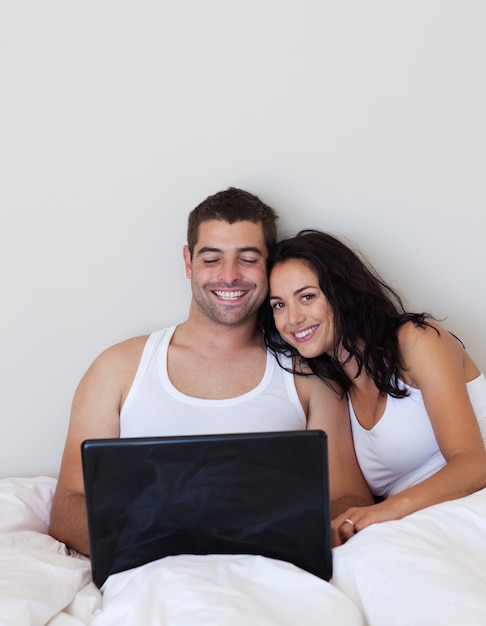 Casal encantado usando um laptop em uma cama