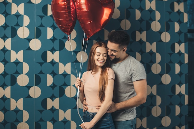 Foto casal encantador se abraçando em uma parede azul segurando balões e namorando no dia dos namorados