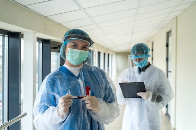 Casal enfermeira vestindo roupas de proteção médica segurando amostras de sangue em tubo de ensaio em clínica moderna