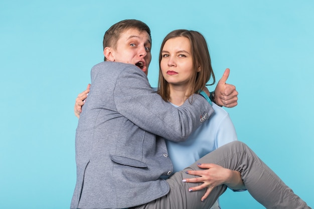 Casal engraçado a brincar - garota mantendo o namorado nas mãos sobre fundo azul.