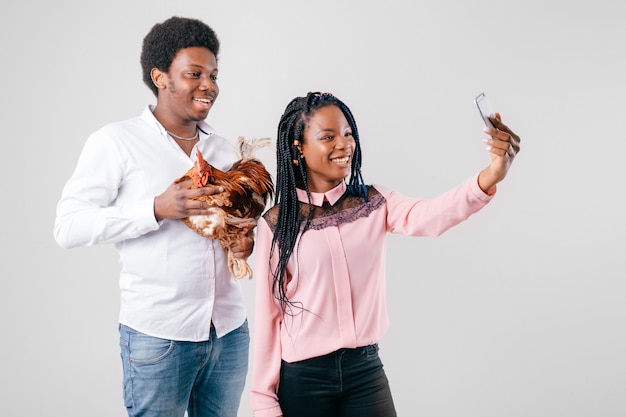 Casal engraçado de pele escura fazendo selfie com frango nas mãos