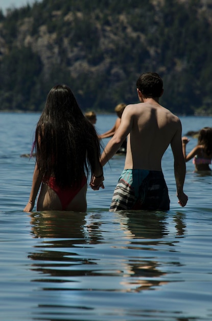 casal entrando na água em um lago com pessoas brincando ao fundo