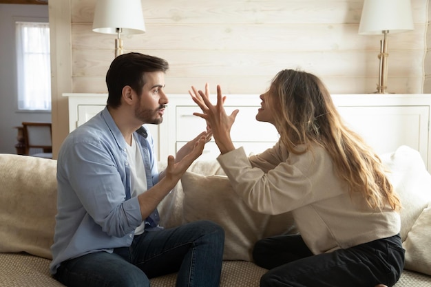 Casal estressado emocionalmente irritado sentado no sofá discutindo em casa Homem irritado irritado mulher nervosa gritando um com o outro descobrindo relações sentindo indignado conceito de problemas de relacionamento