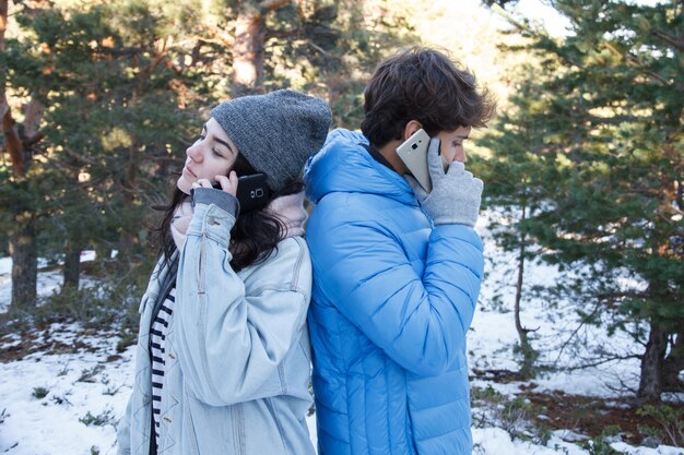 Casal falando no telefone na floresta em um dia nevado.