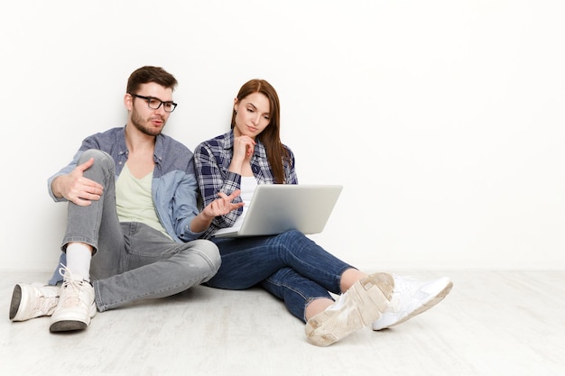 Casal fazendo compras online, fazendo pedidos com um laptop enquanto está sentado na sala de estar vazia