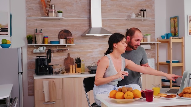 Casal fazendo compras online no laptop durante o café da manhã. inserção de informações, cliente usando tecnologia de e-commerce comprando coisas na web, banco de cosumerismo e pedidos