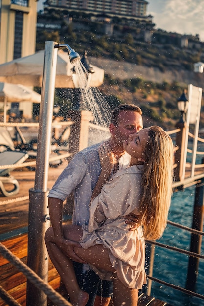 Casal feliz à beira-mar Um cara e uma garota estão debaixo do chuveiro em um píer ao ar livre Casal feliz de férias Homem e mulher à beira-mar