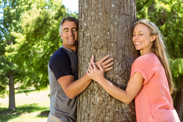Casal feliz abraçando uma árvore